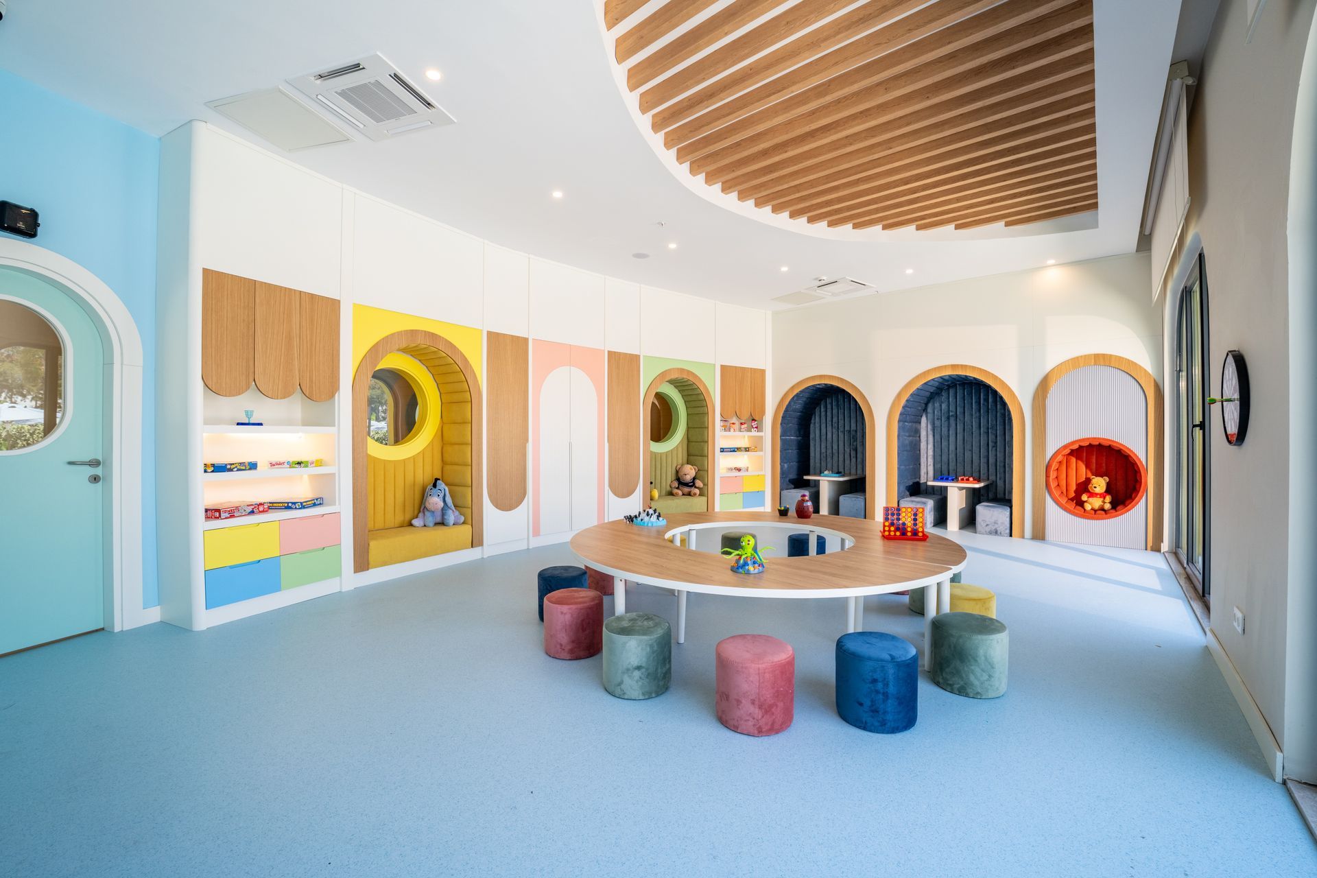 Liu Resorts | Colorful playroom with round table, stools, and arched alcoves with a blue floor and wood accents.