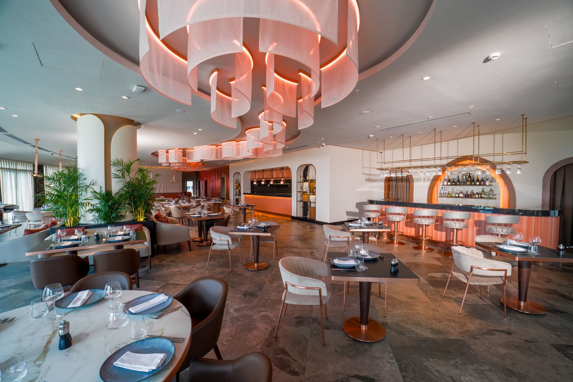 Liu Resorts | Upscale restaurant interior with pink and gold decor, tables set, bar in background.