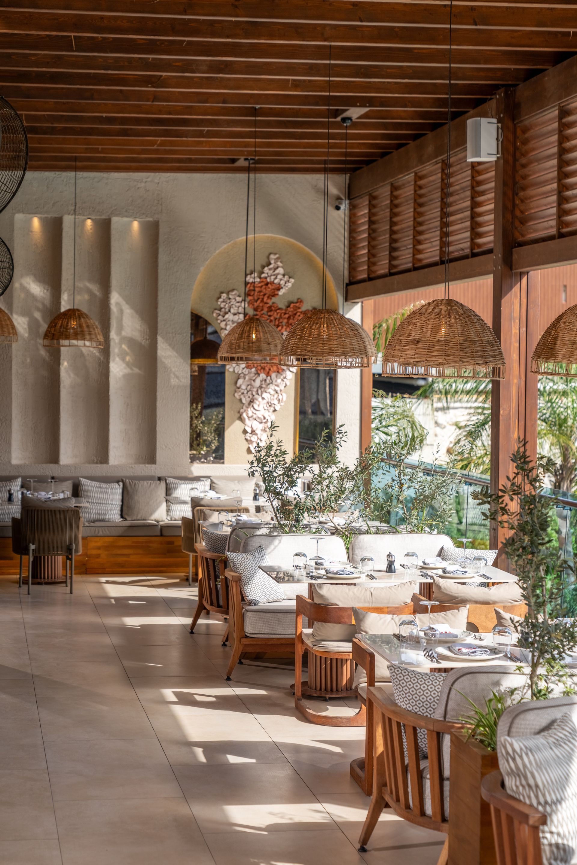 Restaurant interior with wooden beams, tables, chairs, and large windows. Natural light floods the space.