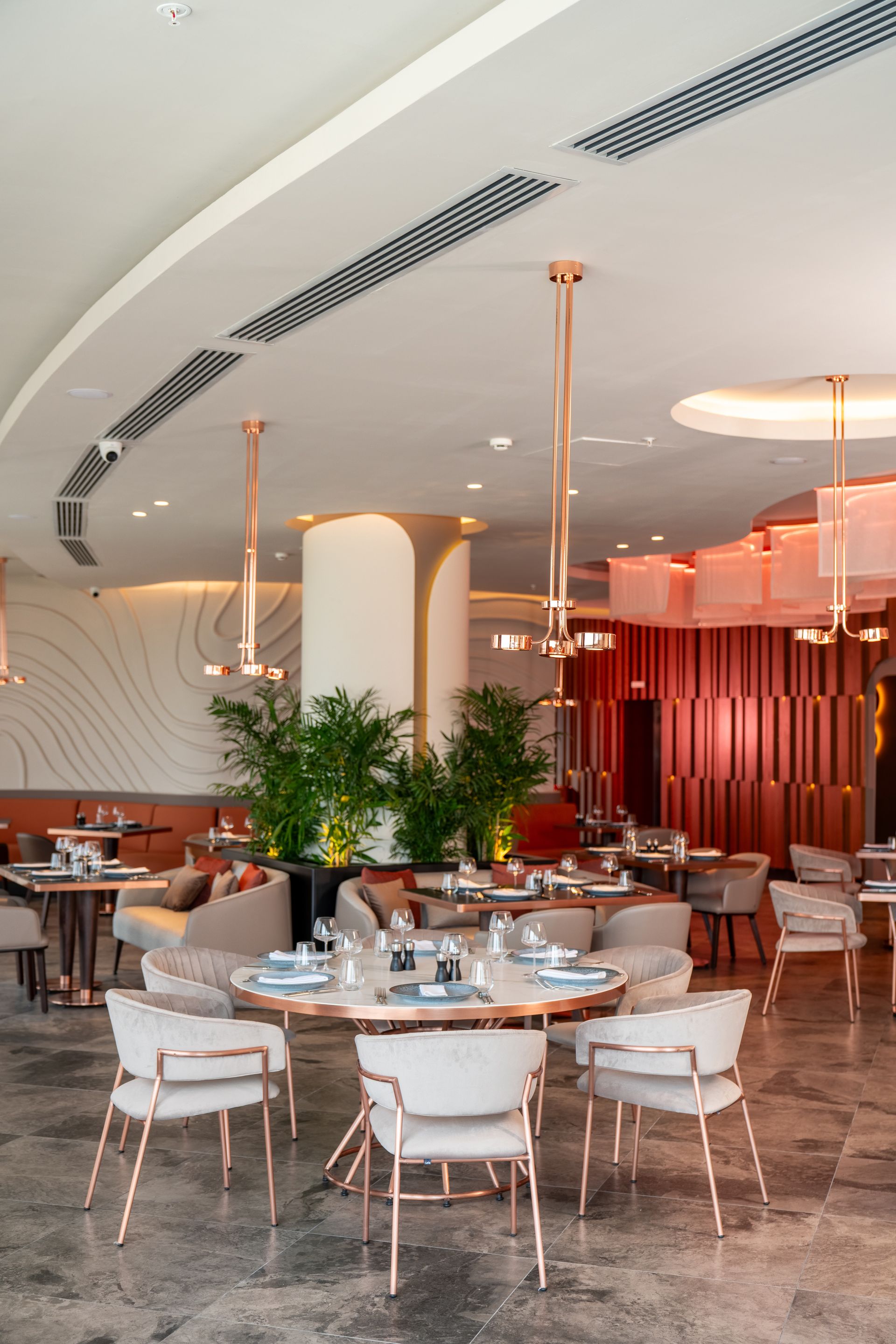 Liu Resorts | Elegant restaurant interior with round tables, chairs, copper accents, and large windows.