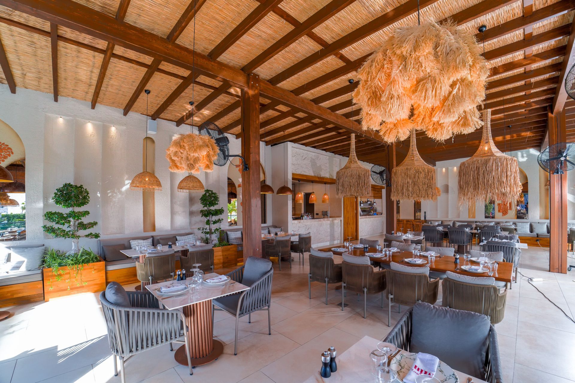 Liu Resorts | Restaurant interior: tables with chairs, hanging woven lights, wood beams, and textured ceiling.