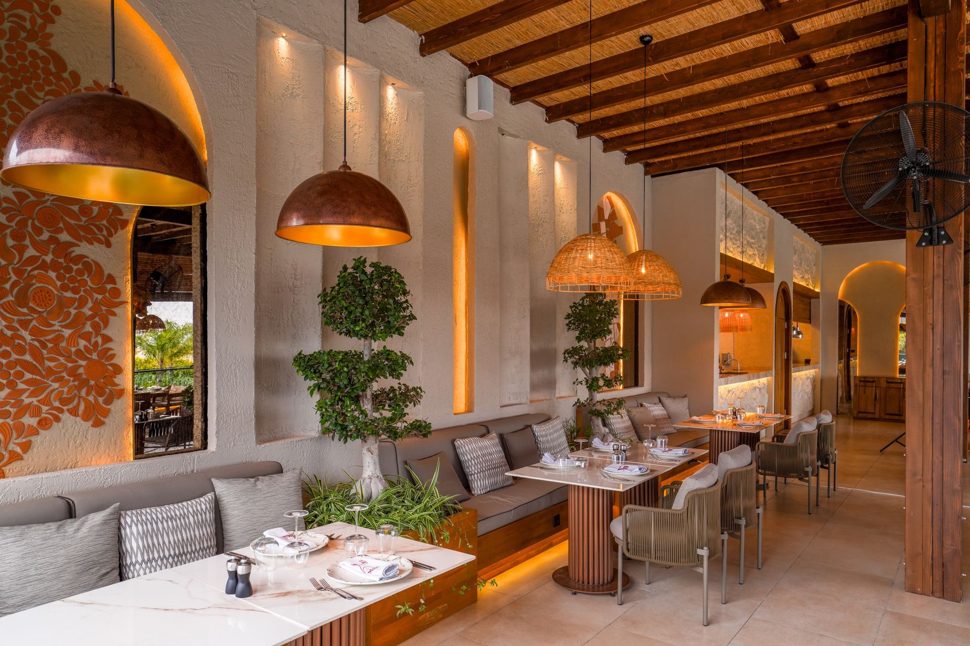 Liu Resorts | Restaurant interior with tables, copper light fixtures, and cushioned seating.