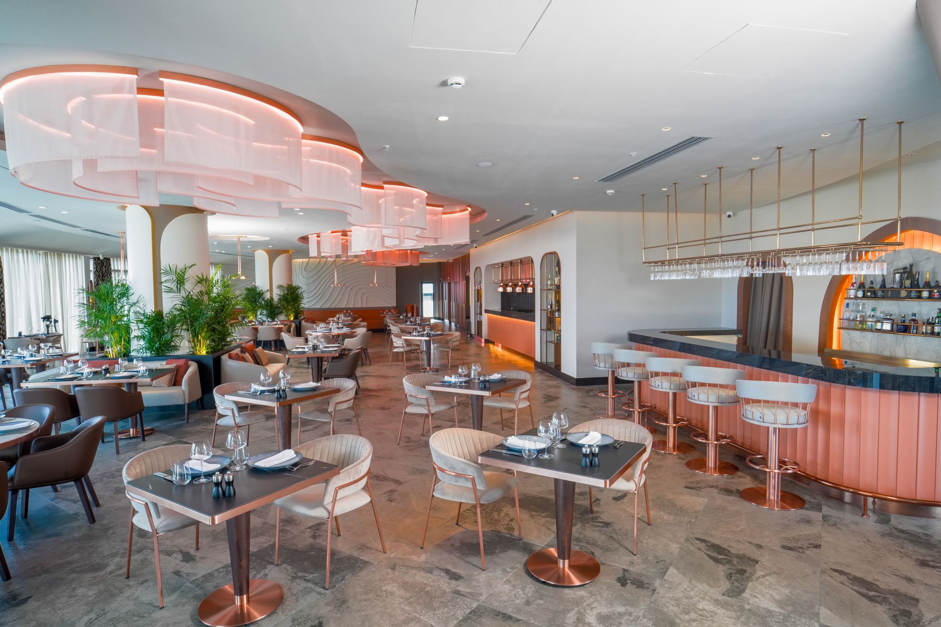 Liu Resorts | Elegant restaurant interior with tables, chairs, bar, and decorative lighting. Copper and cream color scheme.