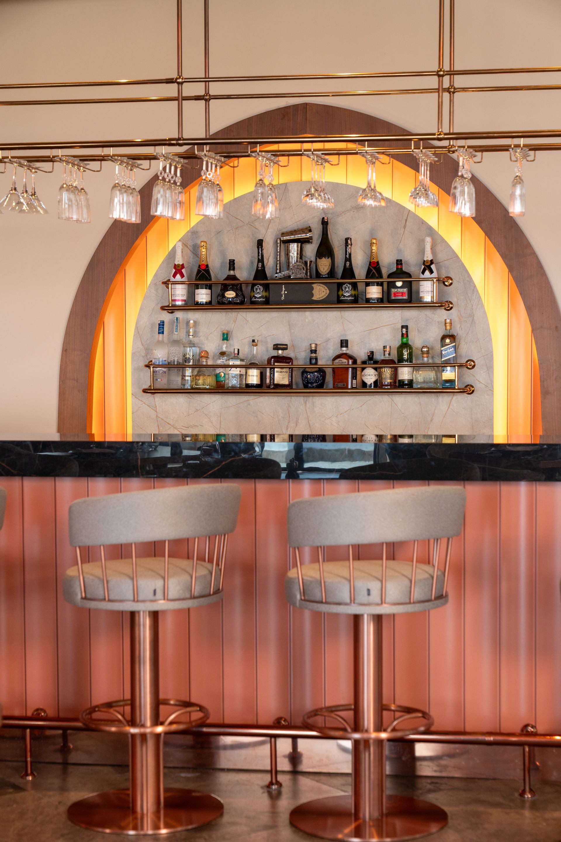 Liu Resorts | A stylish bar with rose-gold accents, stools, and arched back bar displaying bottles and glassware.