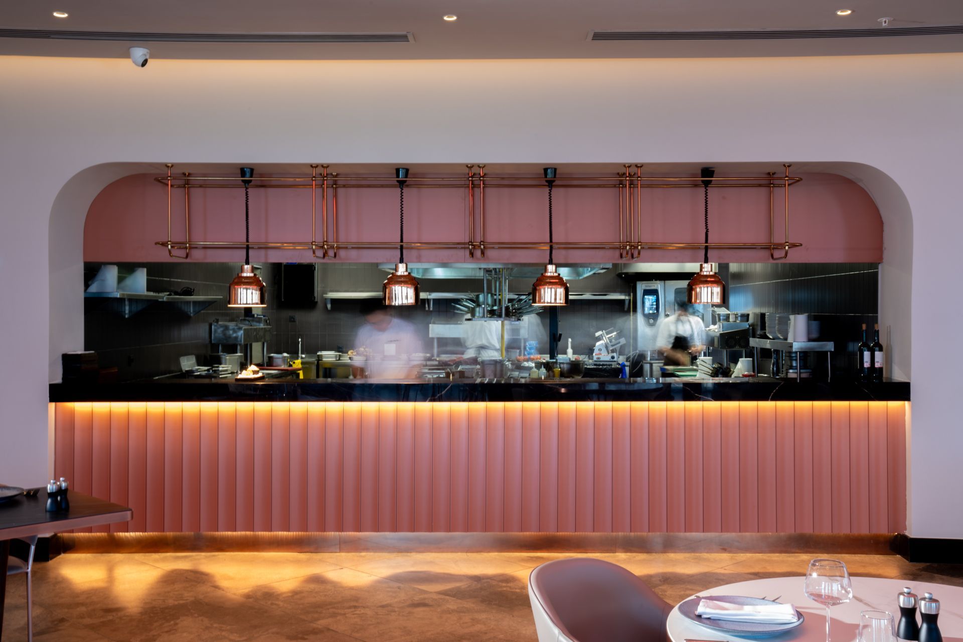 Liu Resorts | Open kitchen with pink accents, chefs at work, overhead copper lighting.