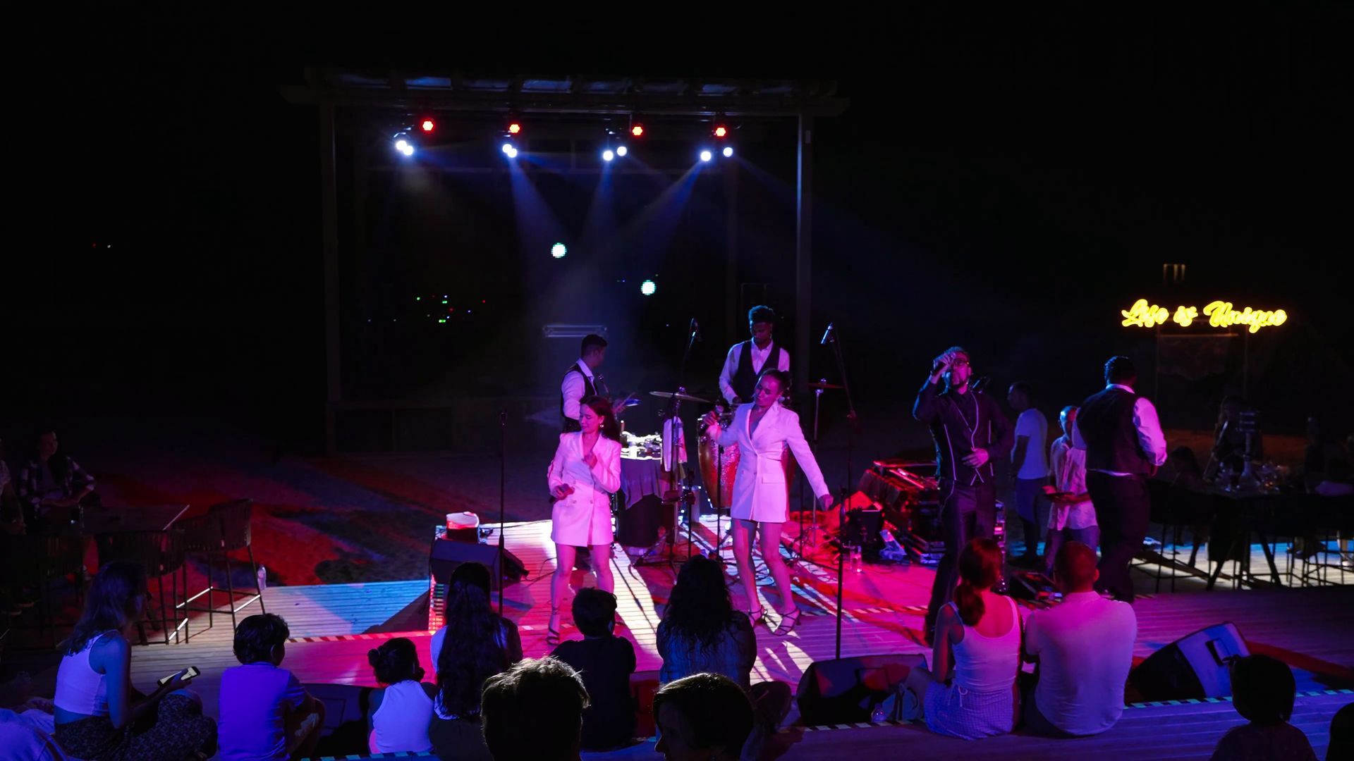 Liu Resorts | Band performing on an outdoor stage at night, lit by spotlights. Audience watches from below.
