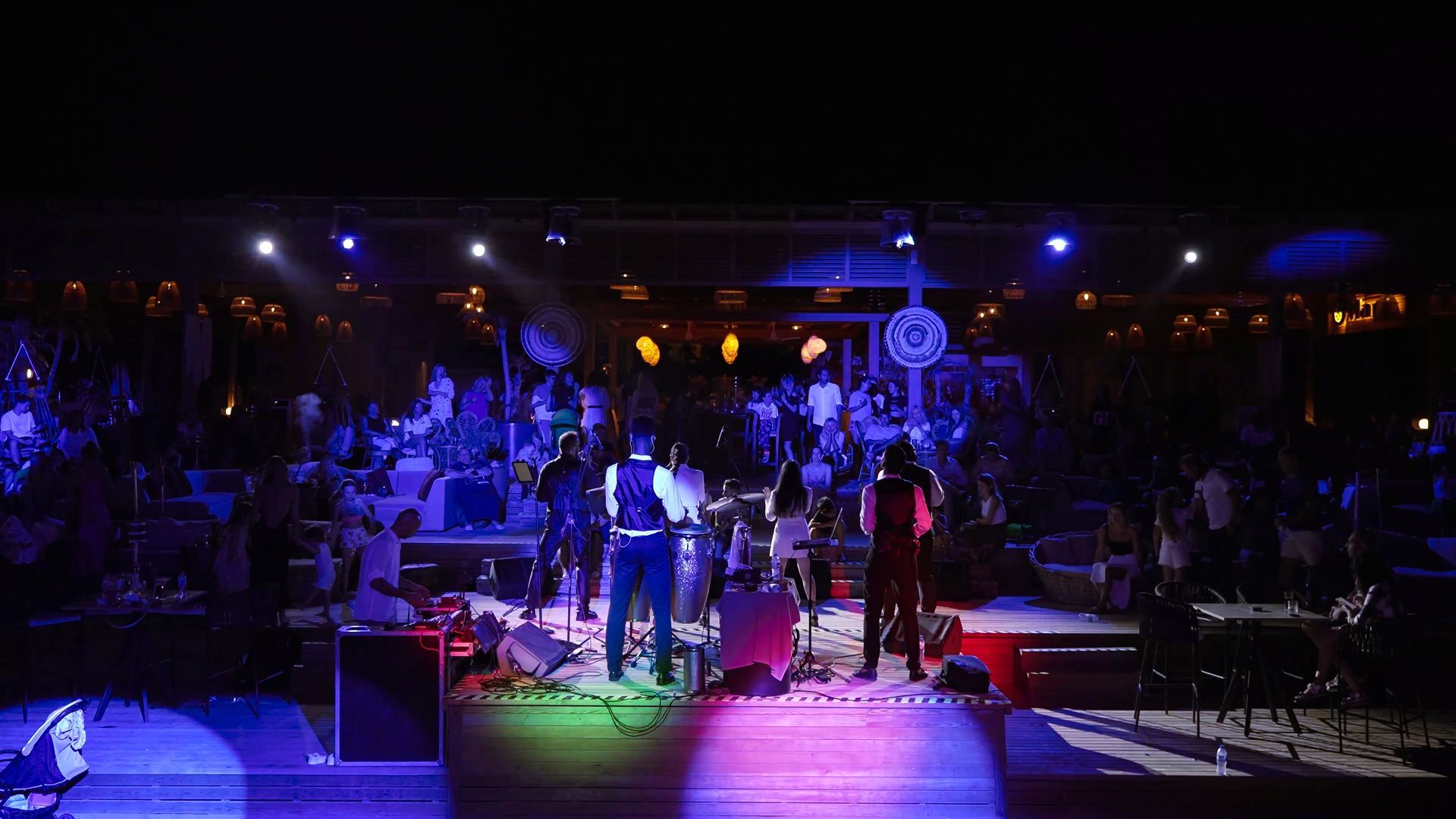 Liu Resorts | Band performing on stage in front of a crowd, lit by colorful stage lights.