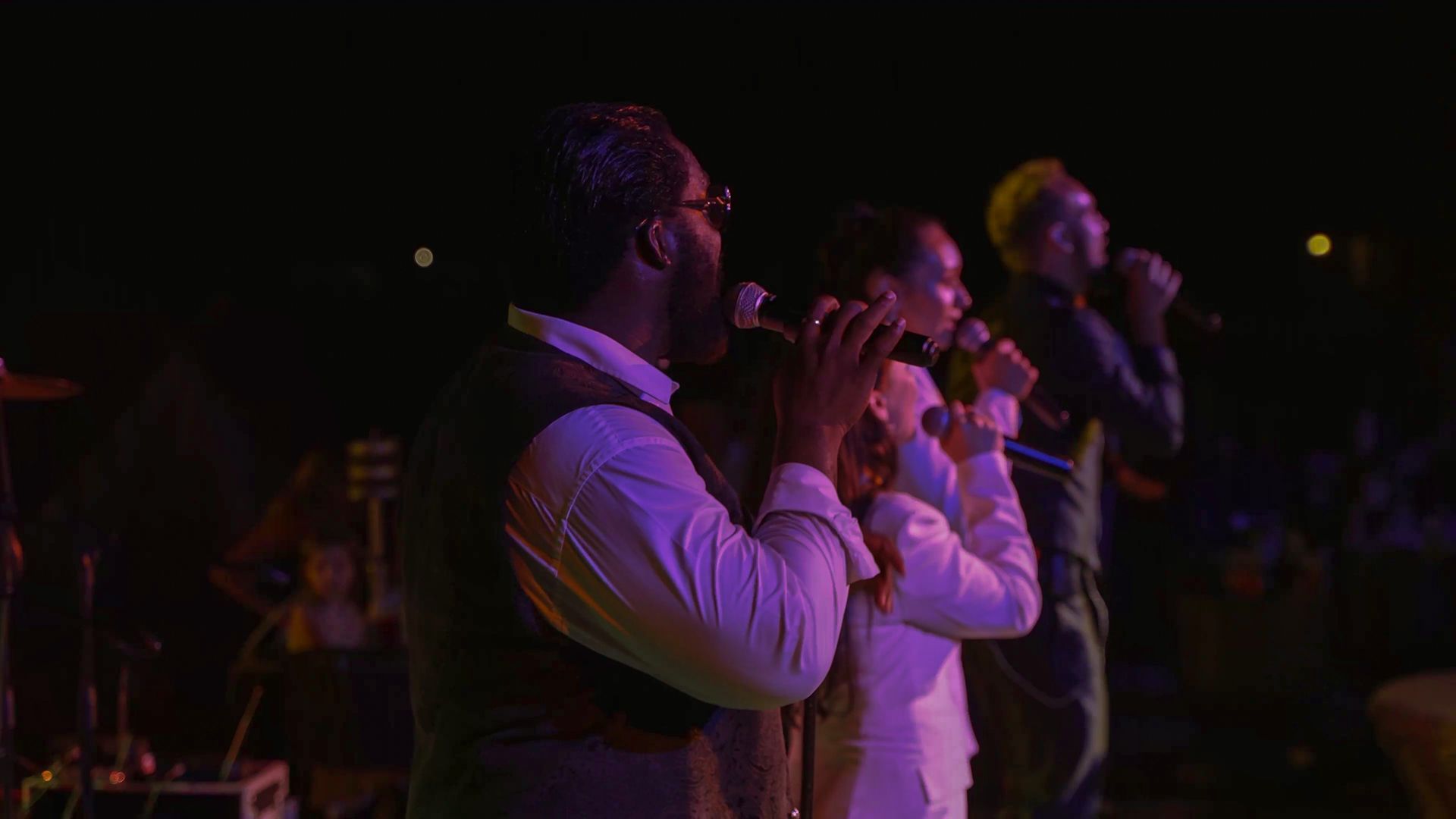Liu Resorts | Three people singing into microphones on stage, lit with purple and green lights.